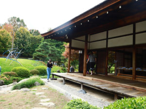 Shofuso's house, a person walking in front of it, the sun is shining.