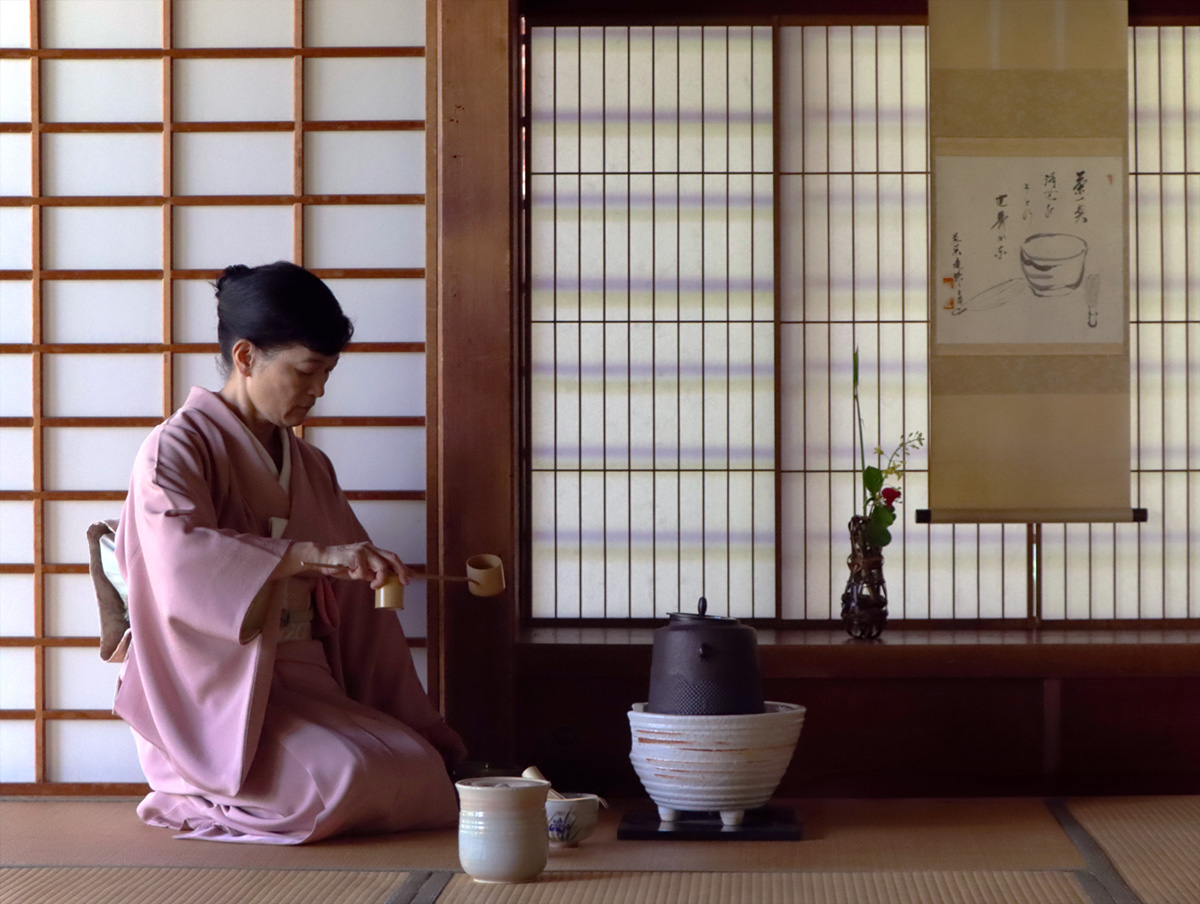 Woman in traditional kimono performing Japanese tea ceremony.